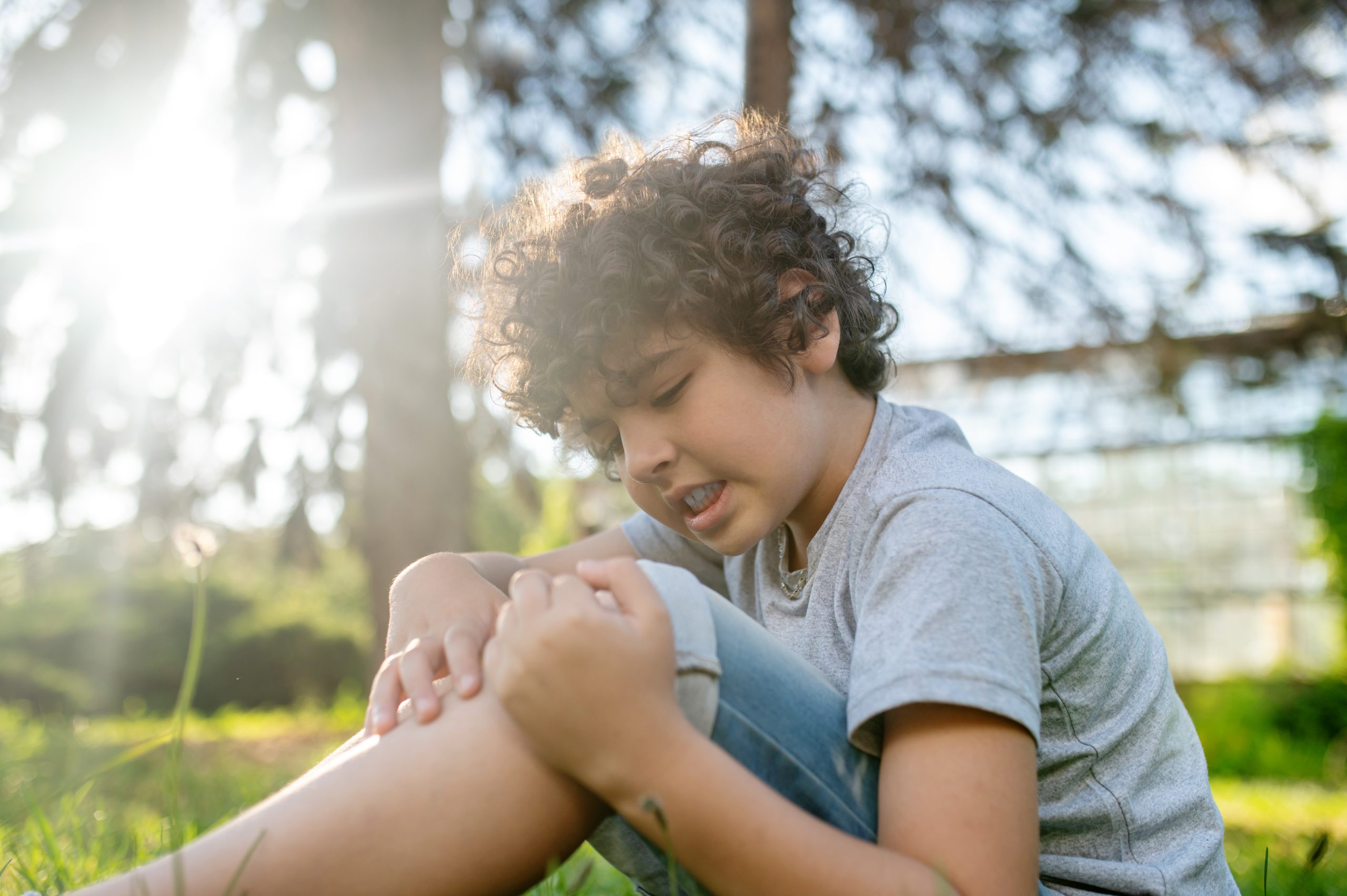 Focused dark-haired boy examining his damaged knee